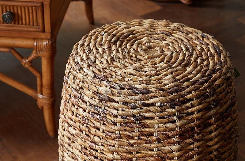 A woven rattan stool with a natural, rustic texture, adding an earthy touch to the wooden floor and furniture in the room. Perfect for bohemian or tropical-inspired interiors